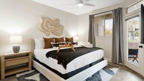 A bedroom with a bed, bedside tables, a ceiling fan, a window with curtains, and a view of the outside.