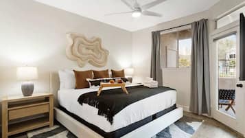 A bedroom with a bed, bedside tables, a ceiling fan, a window with curtains, and a view of the outside.