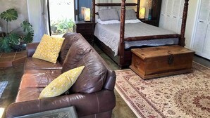 Une chambre à coucher avec un lit à baldaquin, un canapé en cuir marron agrémenté de coussins à motifs, une commode en bois et un tapis à motifs.
