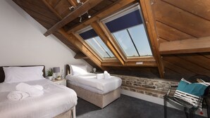 Une chambre avec un plafond en pente, un puits de lumière, un lit, une table de chevet et une chaise.