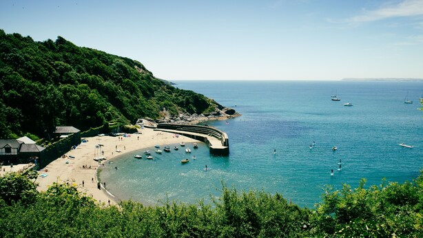 Une plage côtière avec des bateaux, un rivage sablonneux et une colline boisée.