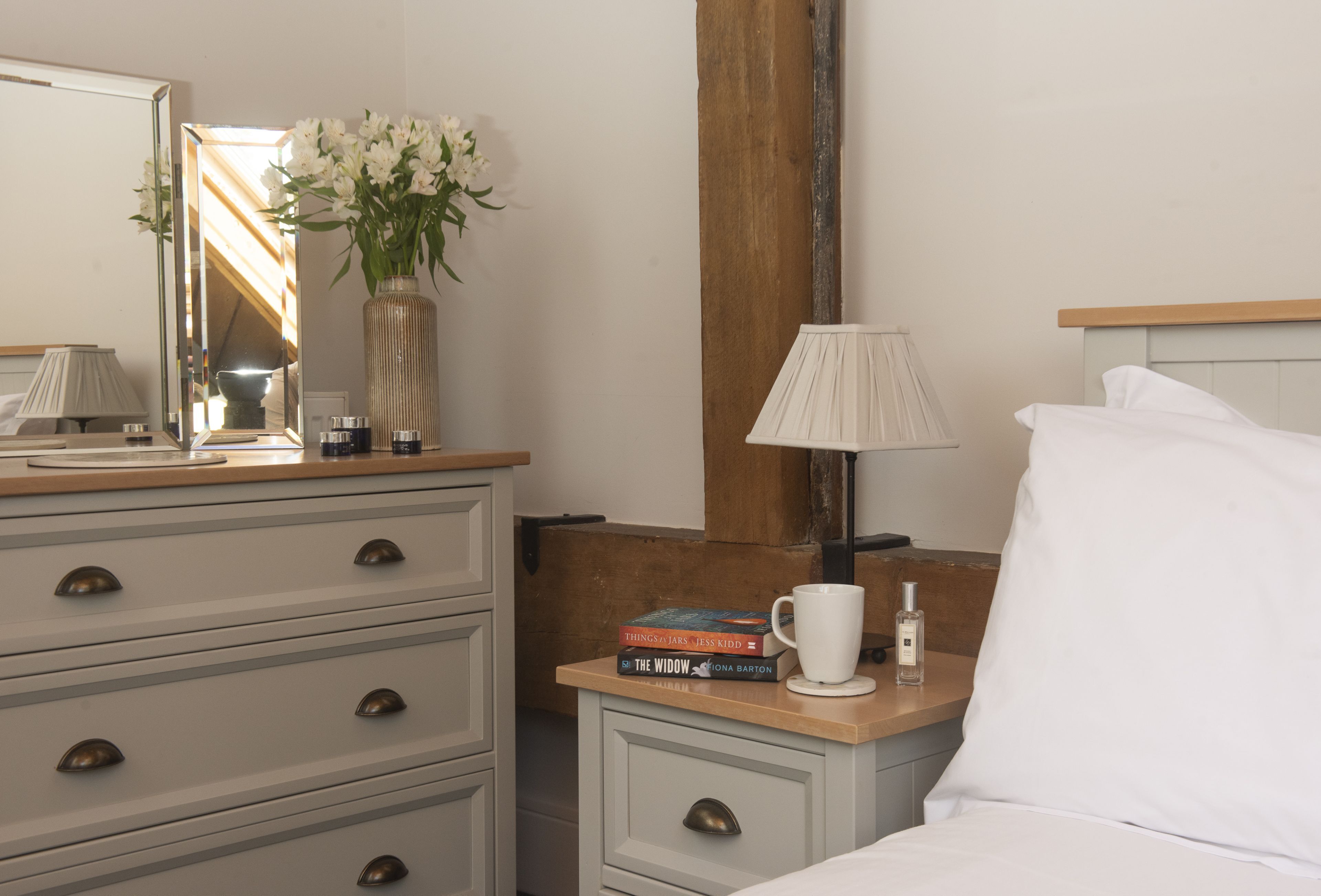 A neatly arranged bedroom with a bed, bedside table, lamp, and a dresser with drawers.