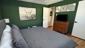 A bedroom with a bed, a dresser, a television, and a door leading to another room. - Crown Hill Retreat - Hot Tub/Yard/Parking (Lakewood)