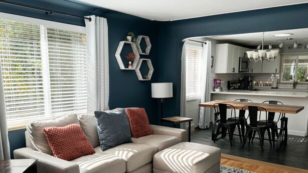 A modern living room with a sectional sofa, a dining area with a wooden table and chairs, and a kitchen in the background. - Crown Hill Retreat - Hot Tub/Yard/Parking (Lakewood)