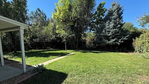 A well-maintained grassy backyard with a covered patio area, surrounded by trees. - Crown Hill Retreat - Hot Tub/Yard/Parking (Lakewood)