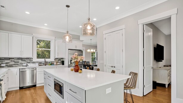 A modern kitchen with white cabinetry, a large island, pendant lighting, and a dining area with a chair.