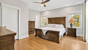 A bedroom with a wooden bed, a ceiling fan, and a window with a view of trees.