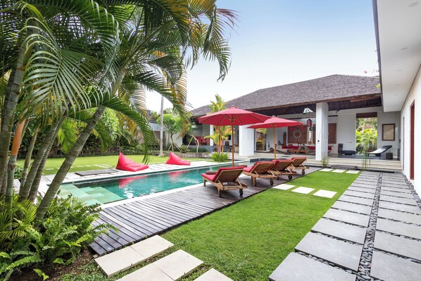 A pool area with lounge chairs and umbrellas, surrounded by palm trees and a well-maintained lawn.