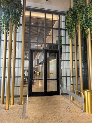 L’entrée d’un hôtel avec une porte en verre, un sol en briques et une rambarde en métal.