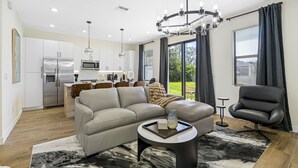 Un salon moderne avec un canapé, une table basse et un fauteuil noir. On aperçoit au fond une cuisine équipée d’un réfrigérateur et d’un four à micro-ondes.