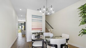 Un espace repas moderne avec une table en verre, des chaises à revêtement blanc, un lustre et un grand tableau abstrait accroché au mur.