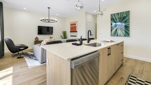 Une cuisine moderne dotée d’un îlot central, d’un lave-vaisselle intégré et de luminaires suspendus.