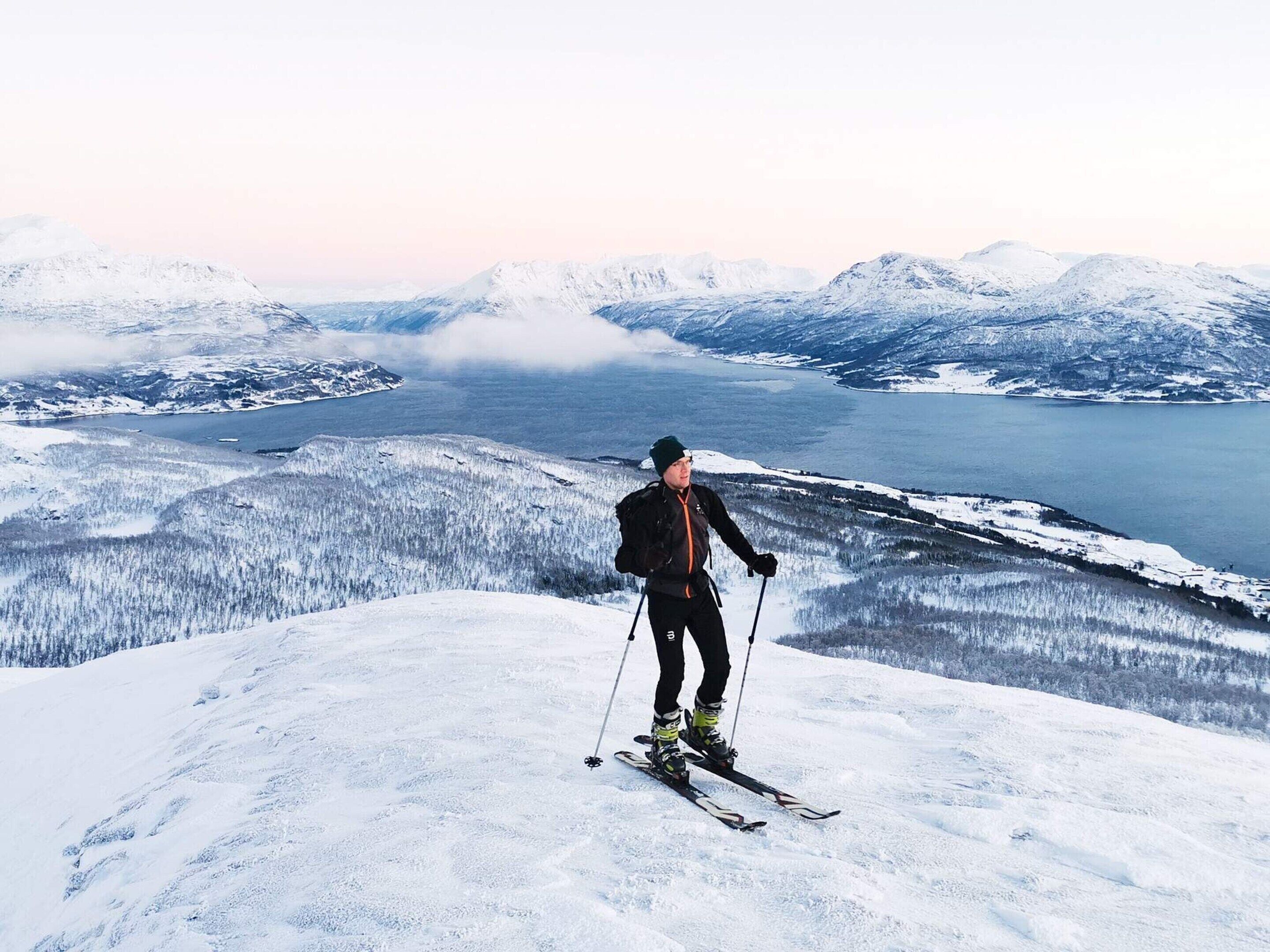 A person skiing on a snow-covered mountain with a lake and snow-covered trees in the background.