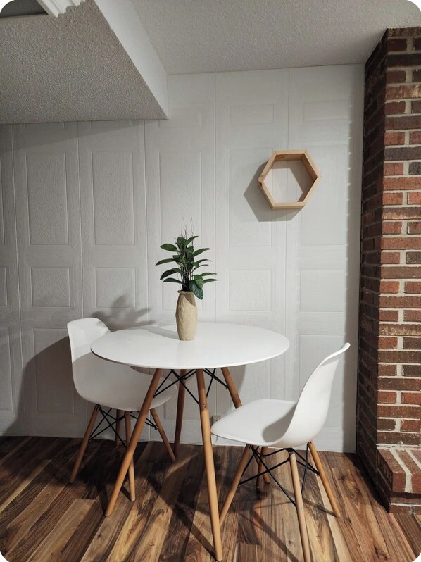 A dining area with a round table, two white chairs, a potted plant, and a hexagonal wooden shelf.