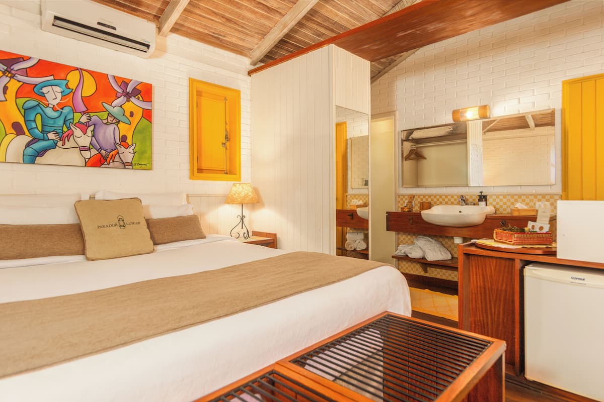 A hotel room with a bed, a bedside table, a lamp, a bathroom with a sink, mirror, and towel rack.