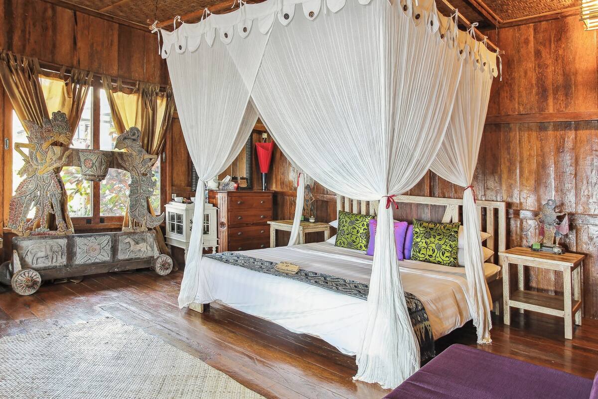 Ein Bett mit Baldachin und weißen Vorhängen, Holzmöbel und Dekoration in einem rustikalen Raum.