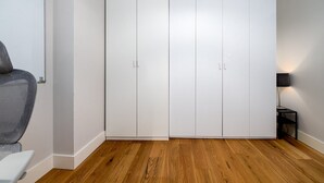 Una habitación con un armario blanco grande, una silla gris y una mesita con una lámpara.