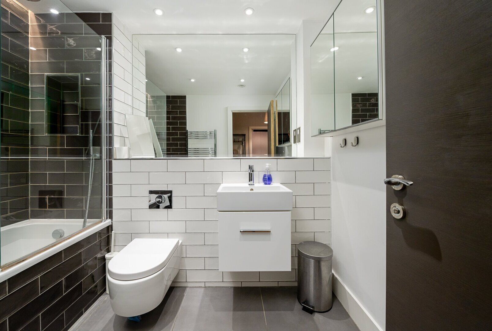 Un bagno moderno con doccia vetrata, un water bianco, un lavandino con specchio sopra e un cestino.