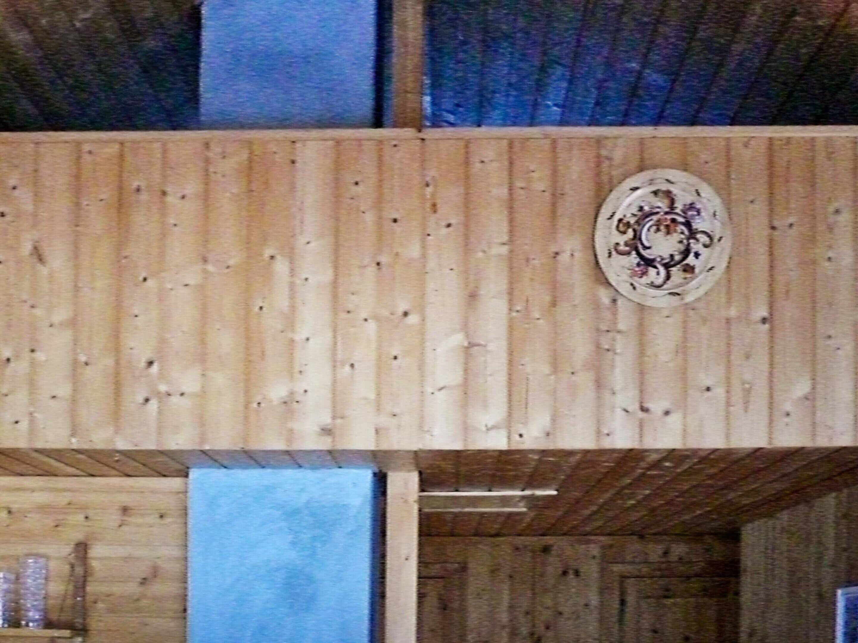 A wooden interior with a decorative plate on the wall, a shelf with jars, and a blue mat on the floor.