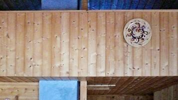 A wooden interior with a decorative plate on the wall, a shelf with jars, and a blue mat on the floor.