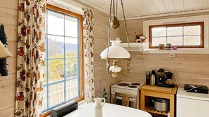 A cozy kitchen with a table, a hanging light fixture, a stove, and a window with curtains. - 5 Person Holiday Home in Akra (Kvinnherad)