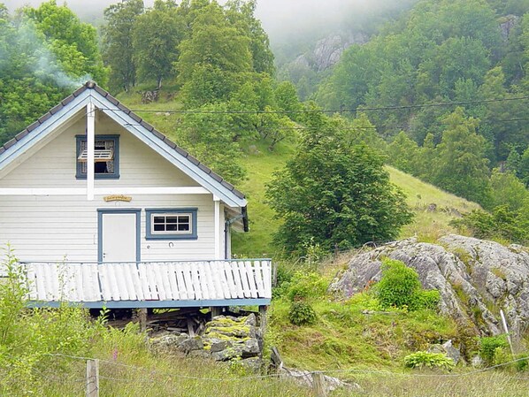 A white wooden house with a gabled roof, a front porch, and a small window. - 5 Person Holiday Home in Akra (Kvinnherad)