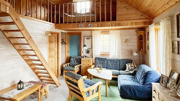 A wooden cabin with a loft bedroom, a living room with a sofa and chairs, and a staircase. - 5 Person Holiday Home in Akra (Kvinnherad)