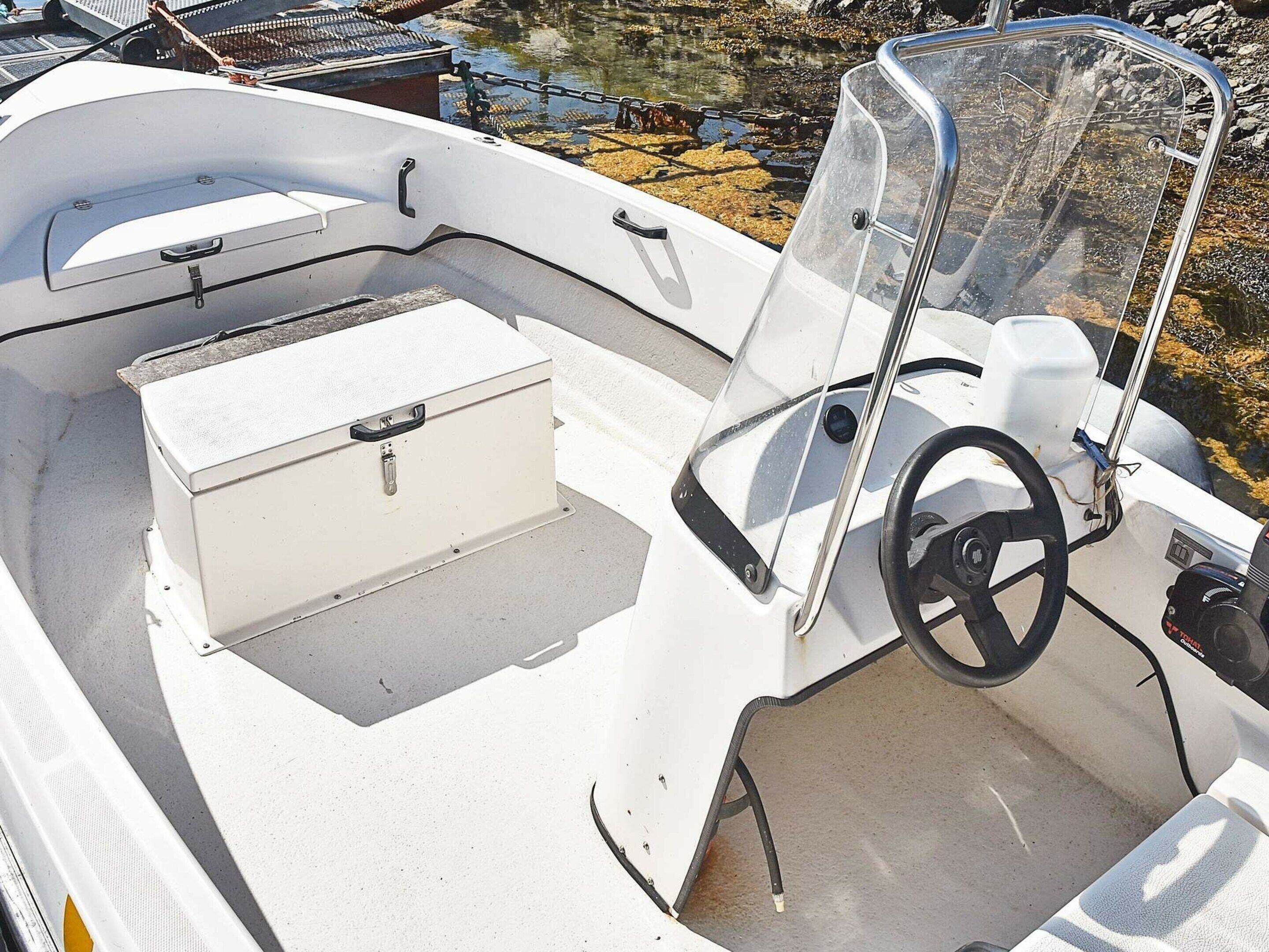 Interior de un barco con timón, un asiento acolchado y un baúl de almacenamiento.