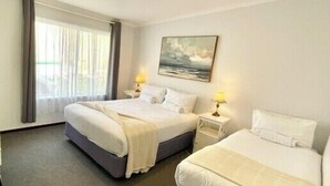 Quarto de hotel com duas camas, uma janela grande com cortinas, um quadro na parede e abajures.
