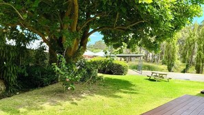 Um deck de madeira com mesa de piquenique e área coberta para sentar num jardim exuberante.