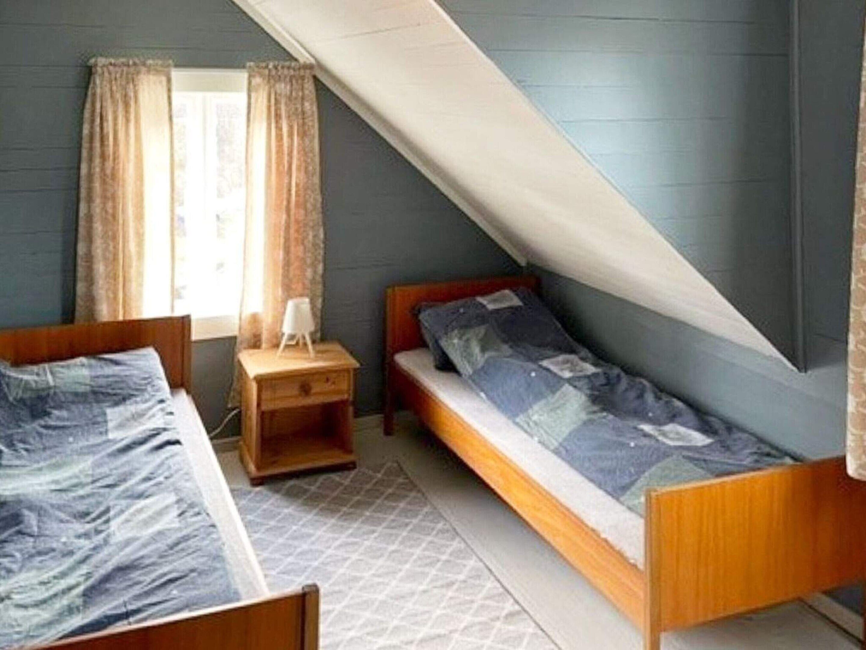 Ein Schlafsaalzimmer mit zwei Betten, einem kleinen Nachttisch und einem Fenster mit Vorhängen.