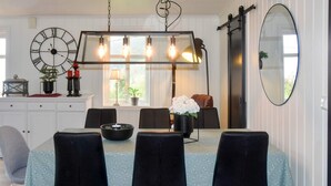 A dining area with a table set for four, black chairs, a large wall clock, and a modern pendant light fixture. - 4 Star Holiday Home in Aram (Vanylven)