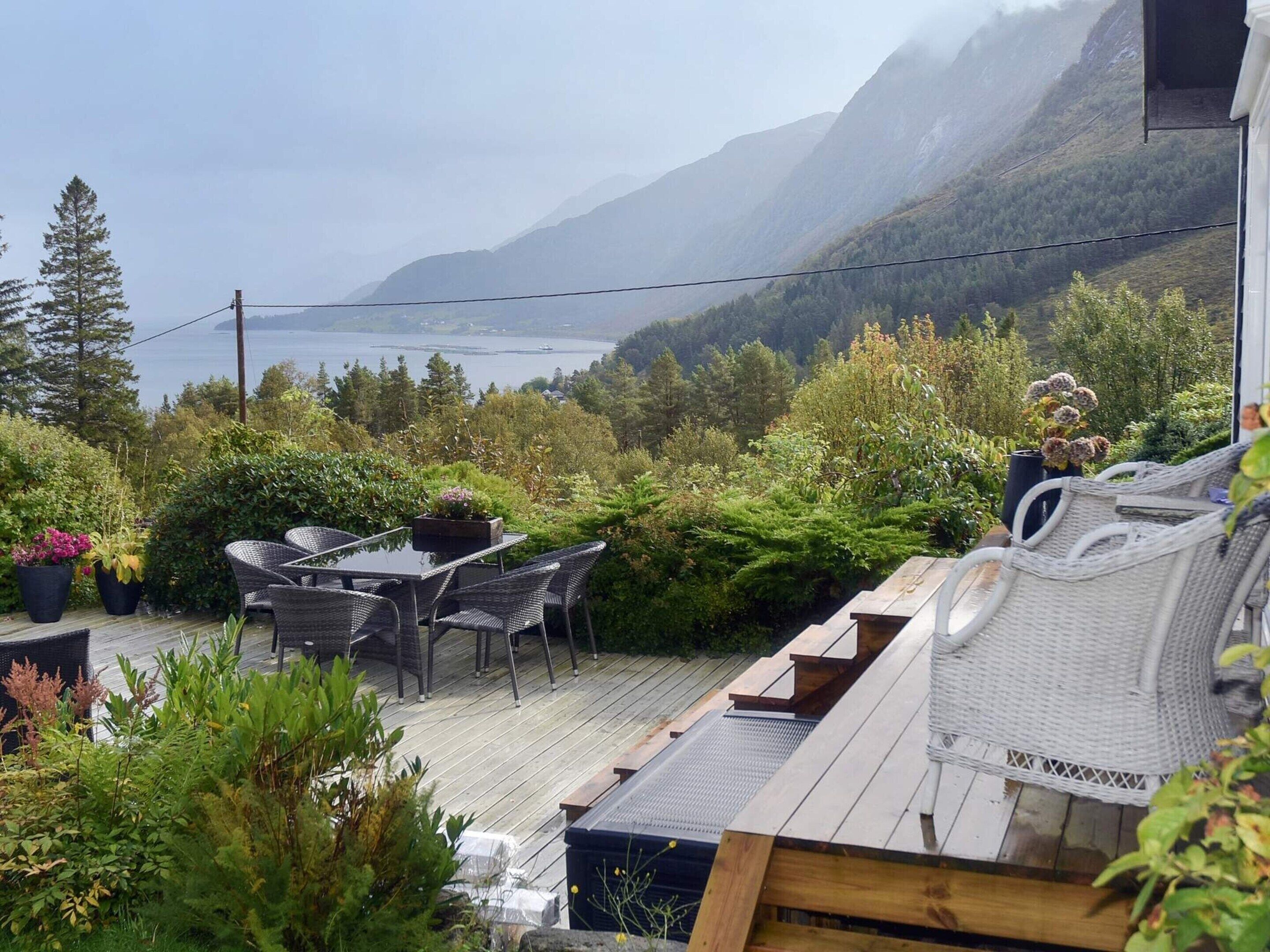 A deck with outdoor furniture overlooking a mountainous landscape and a body of water.