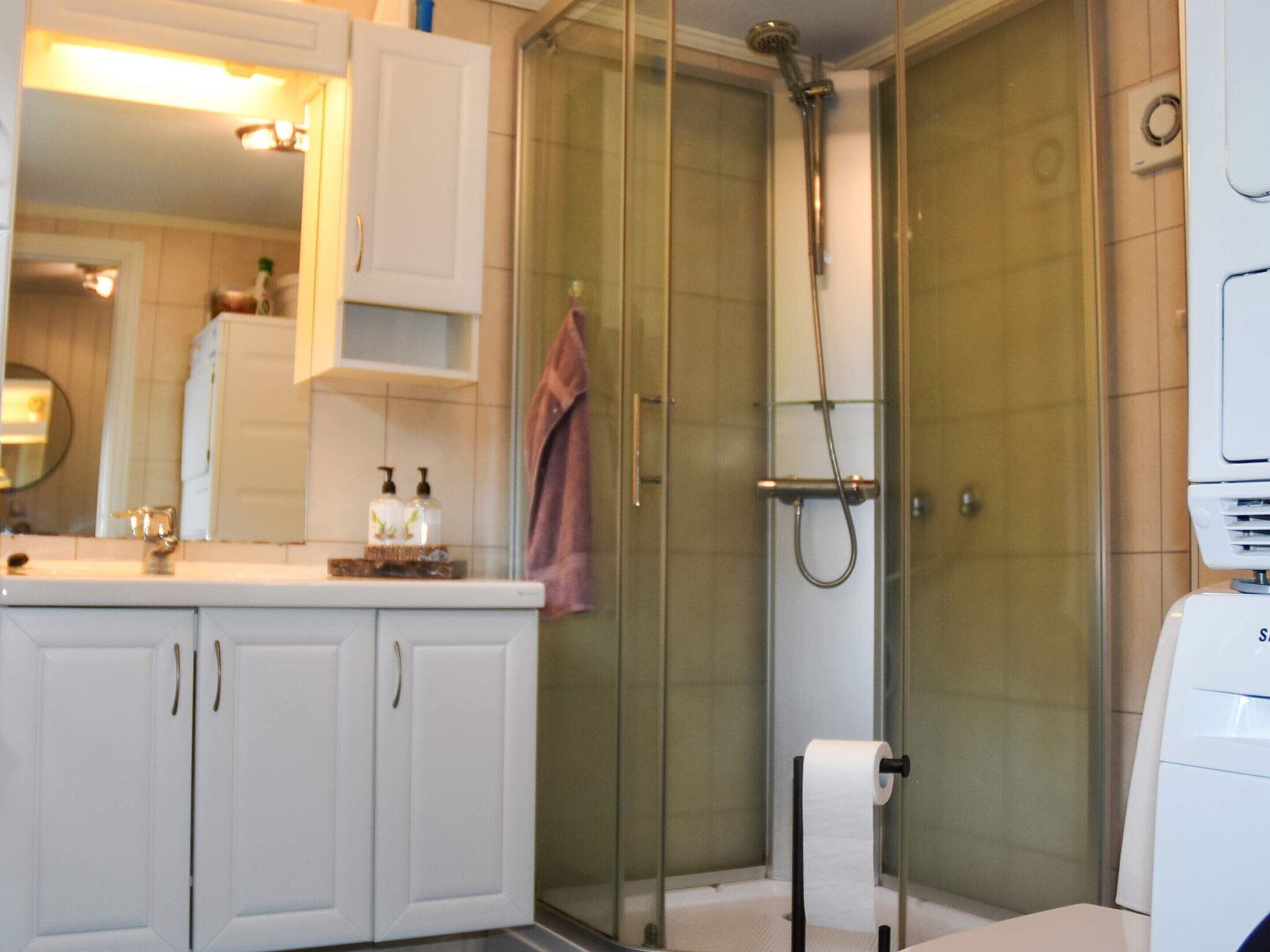 A bathroom with a glass-enclosed shower, a white sink with a mirror above it, and a towel hanging on the wall.