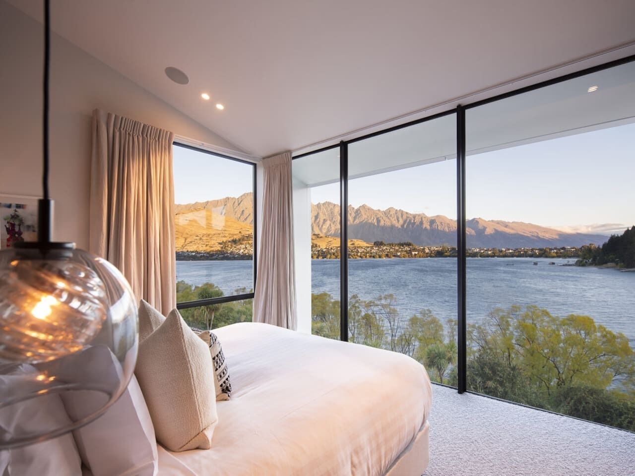 Een slaapkamer met een groot bed, uitzicht op een meer en bergen, en een modern design.
