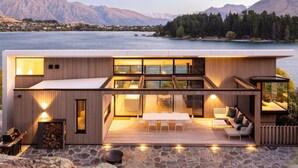 Ein modernes Haus mit Terrasse, das auf einen See blickt, mit Essbereich und einer Sitzecke mit Bergblick.