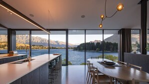 Eine moderne Küche mit einer großen Kochinsel, ein Essbereich mit Blick auf einen See und Berge, und ein großes Fenster, das für natürliches Licht sorgt.