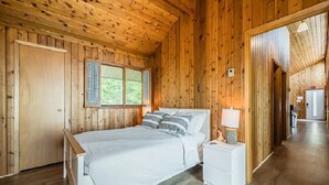Een houten slaapkamer met een bed, nachtkastjes en een raam met luiken.
