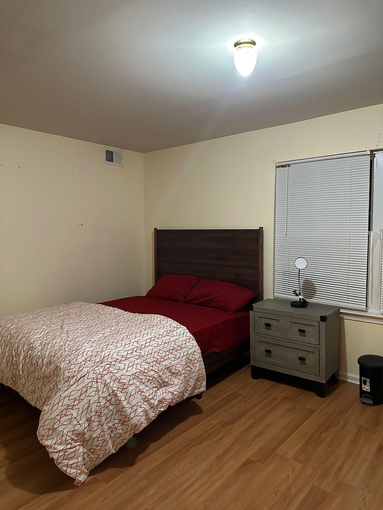 Ein Schlafzimmer mit Bett, Nachttisch, Spiegel und einem Fenster mit Jalousien.