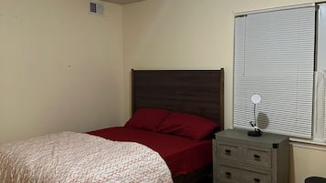 Ein Schlafzimmer mit Bett, Nachttisch, Spiegel und einem Fenster mit Jalousien.