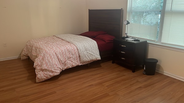 A bedroom with a bed, a nightstand, a lamp, and a window with blinds. - NWK 457 ROOM 111-A (Newark)
