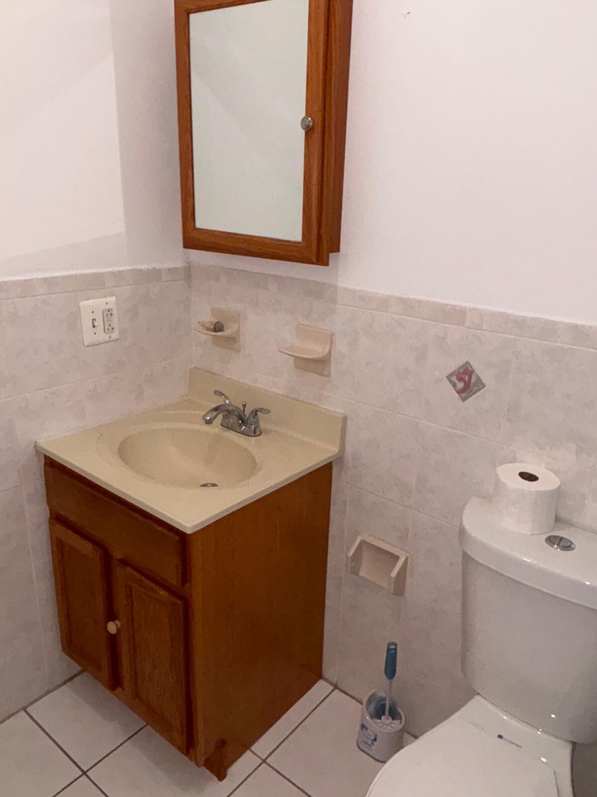 A bathroom with a wooden vanity, a sink, a mirror, a toilet, and a small trash bin.