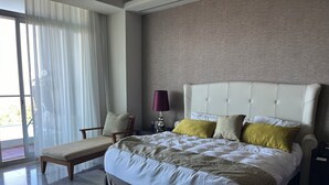 Une chambre d’hôtel avec un grand lit, une chaise, une lampe et une vue sur l’extérieur, visible à travers une porte vitrée.