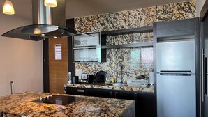 Une cuisine moderne dotée de plans de travail en granit, d’appareils électroménagers en acier inoxydable et de luminaires suspendus.