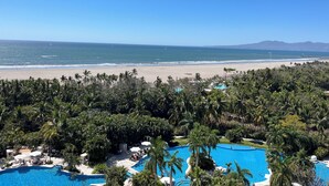 Un complexe hôtelier doté d’une grande piscine entourée de palmiers, d’une plage et offrant une vue sur l’océan.