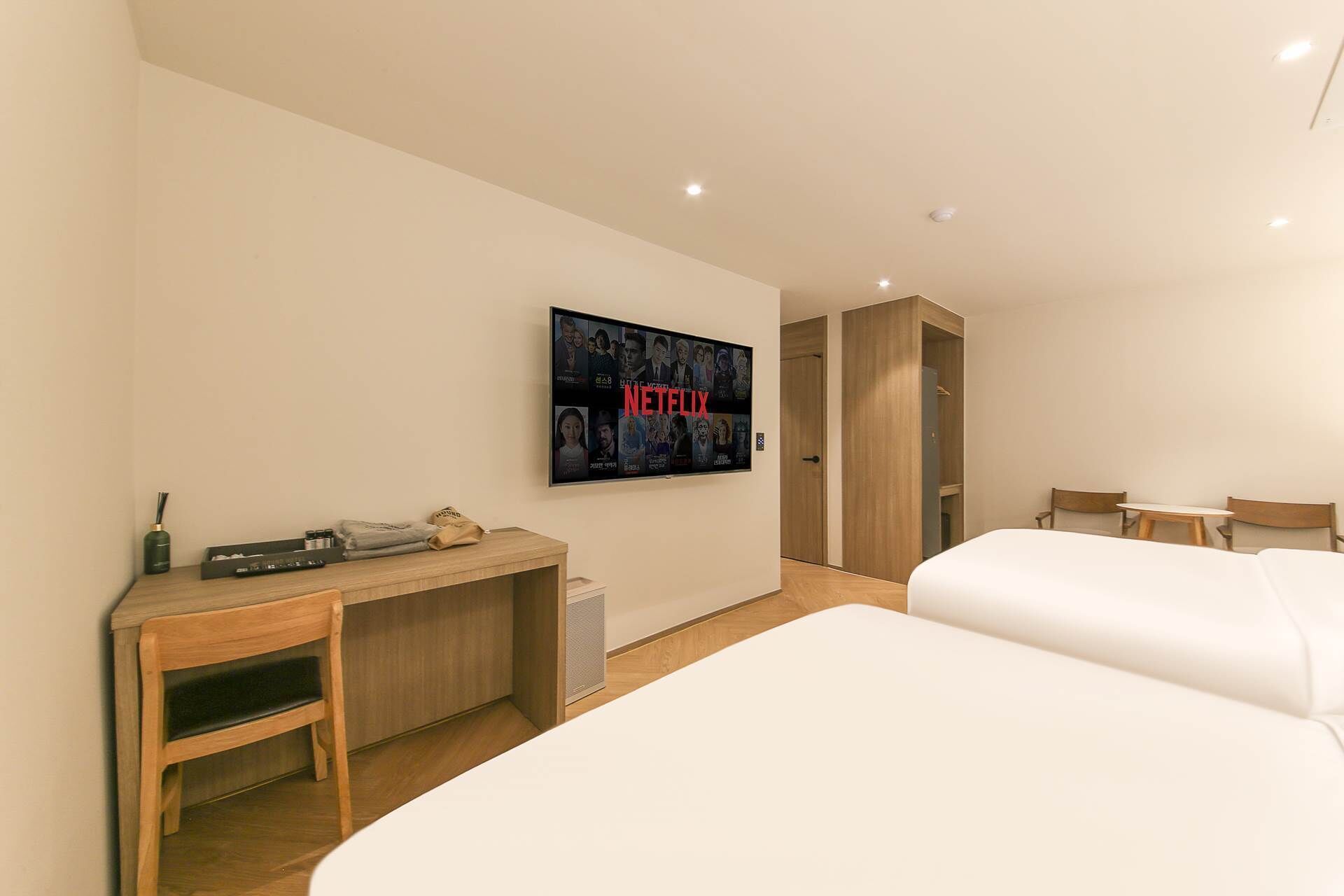A modern hotel room with a large bed, a wooden desk, a television mounted on the wall, and a wardrobe.