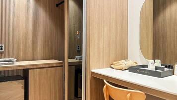 Una habitación de hotel moderna con un panel de pared de madera, un escritorio blanco con espejo, una pequeña silla de madera y un minibar.