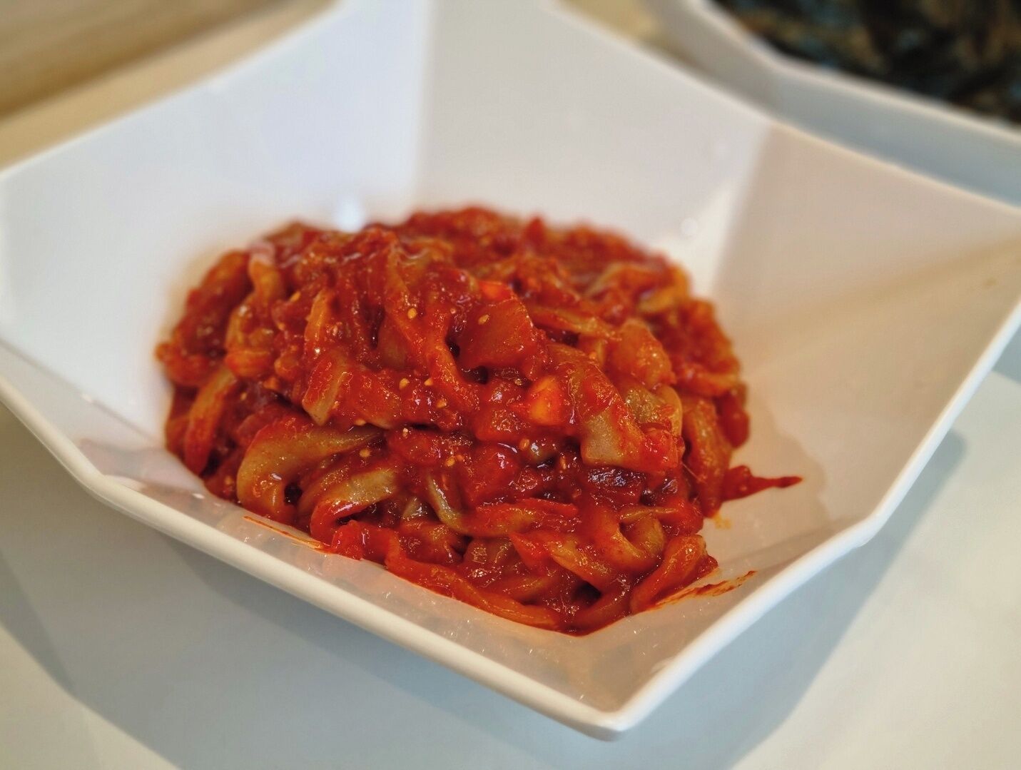 A white bowl containing a red, saucy dish with visible vegetables.