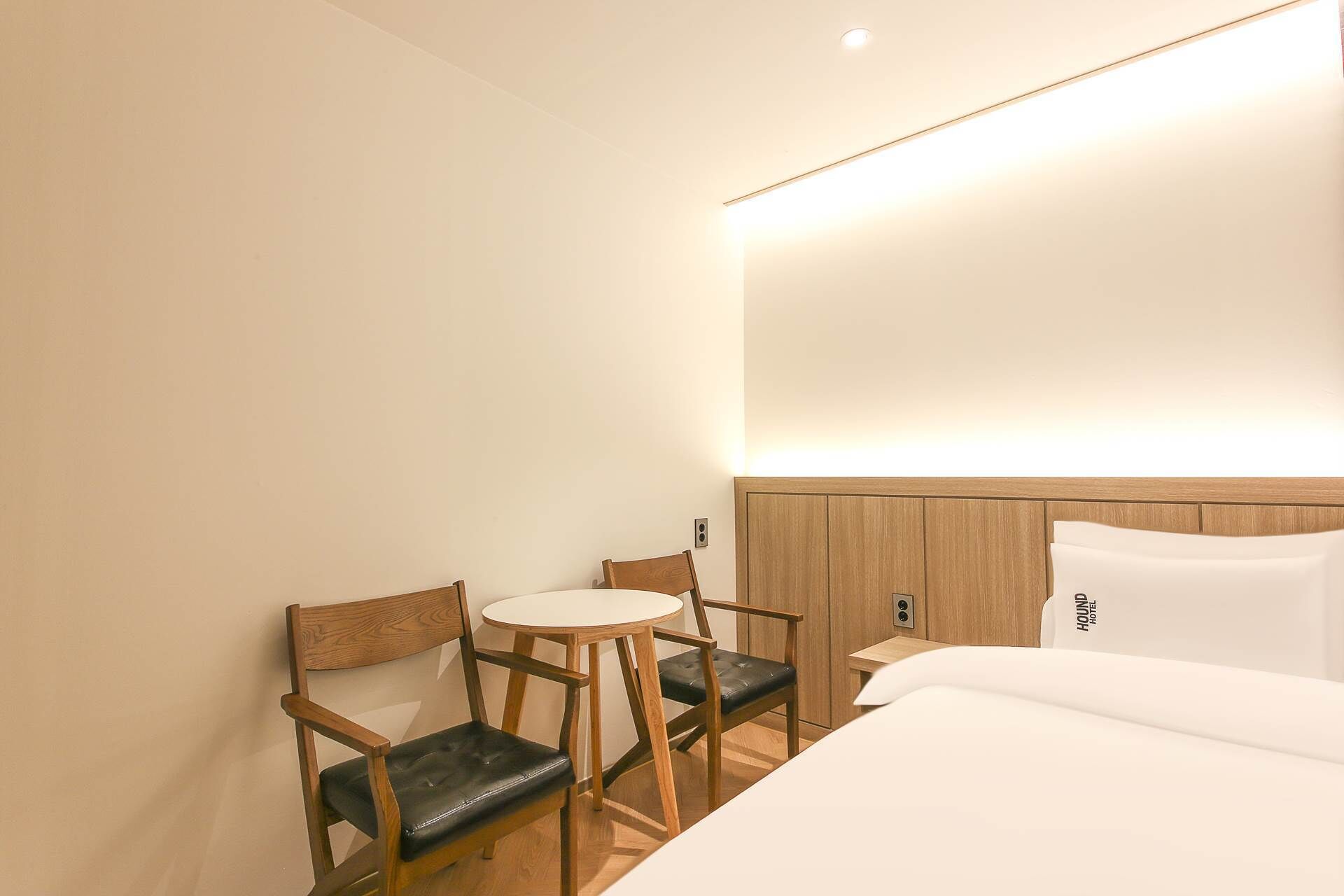 A hotel room with a bed, two wooden chairs, a small round table, and a wall-mounted light fixture.