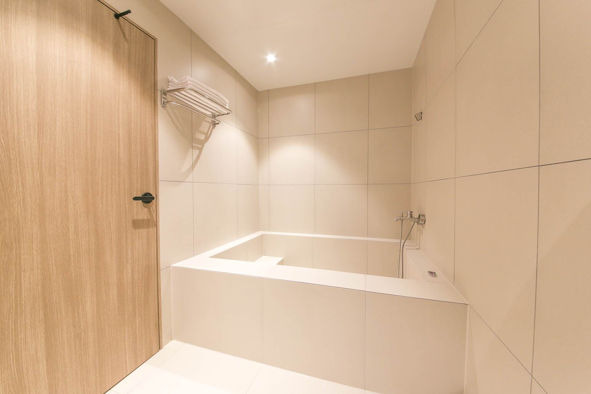 A modern bathroom with a wooden door, a white bathtub, and a towel rack.